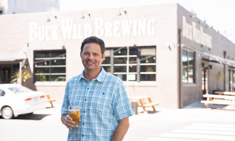 Buck Wild Brewing owner Michael Bernstein stands in front of his brewery in Oakland CA holding a beer.