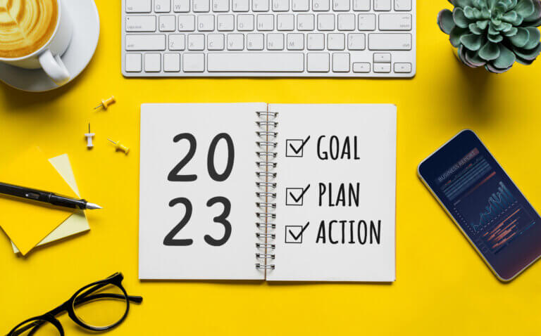 A graphic with an all yellow background with a 2023 action plan calendar, cell phone, keyboard, glasses, and notepad.