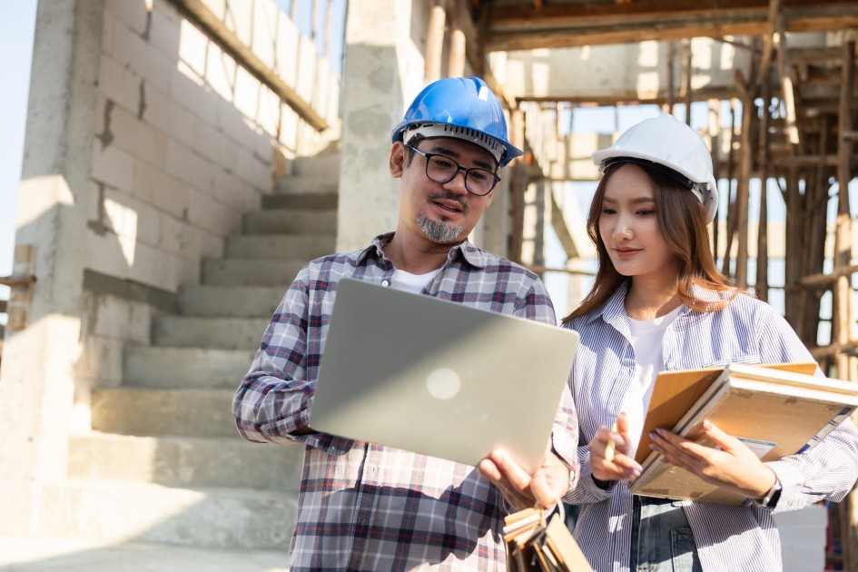 couple collaborating on a construction site, wearing safety gear and discussing plans amidst building materials.