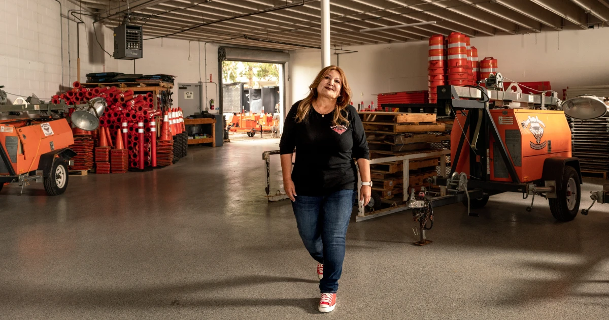 Terry Quinones, dressed in a black shirt and jeans, walks through her warehouse building with equipment in background.