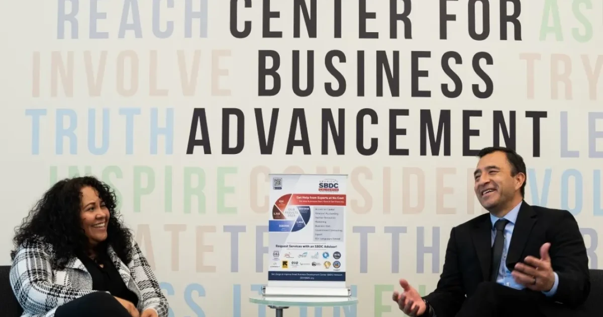 Joel Sedeno and a small business loan officer at CDC Small Business Finance share a joyful moment in the SBDC lobby, engaged in conversation and laughter.