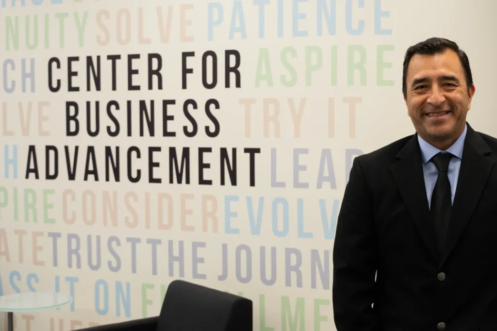A smiling Joel Sedeño poses in front of the SBDC lobby, representing small business support.