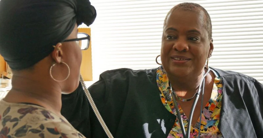 A woman speaks to another woman in a medical setting, conveying concern and support.