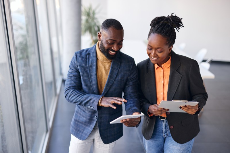 Business owner meeting with a lender partner at their place of business, reviewing information on a tablet in a new, modern building.