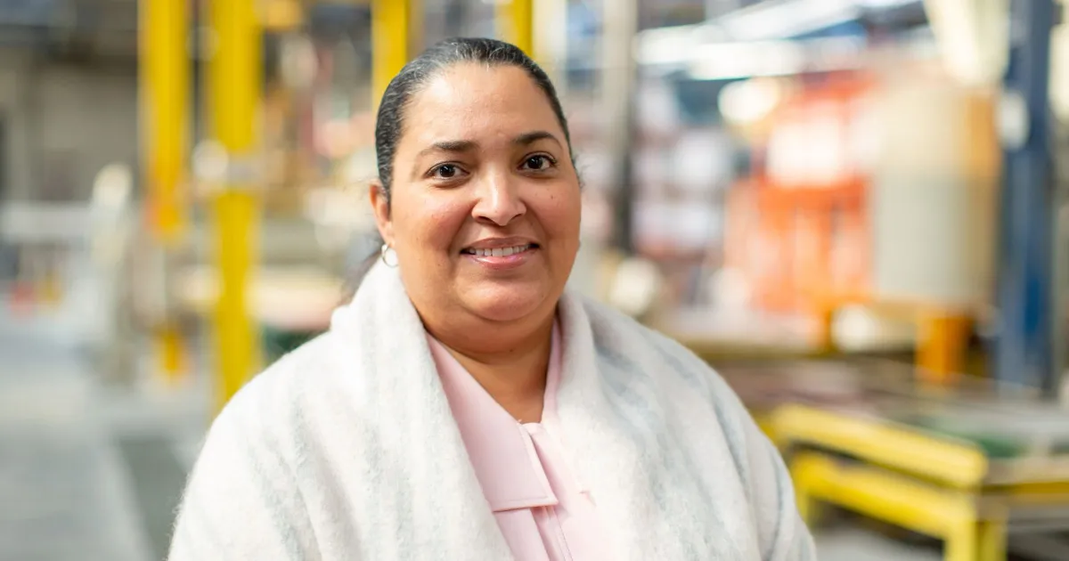 A smiling woman in a factory, representing success in business, featured in a blog post about SBA 504 loan timelines.